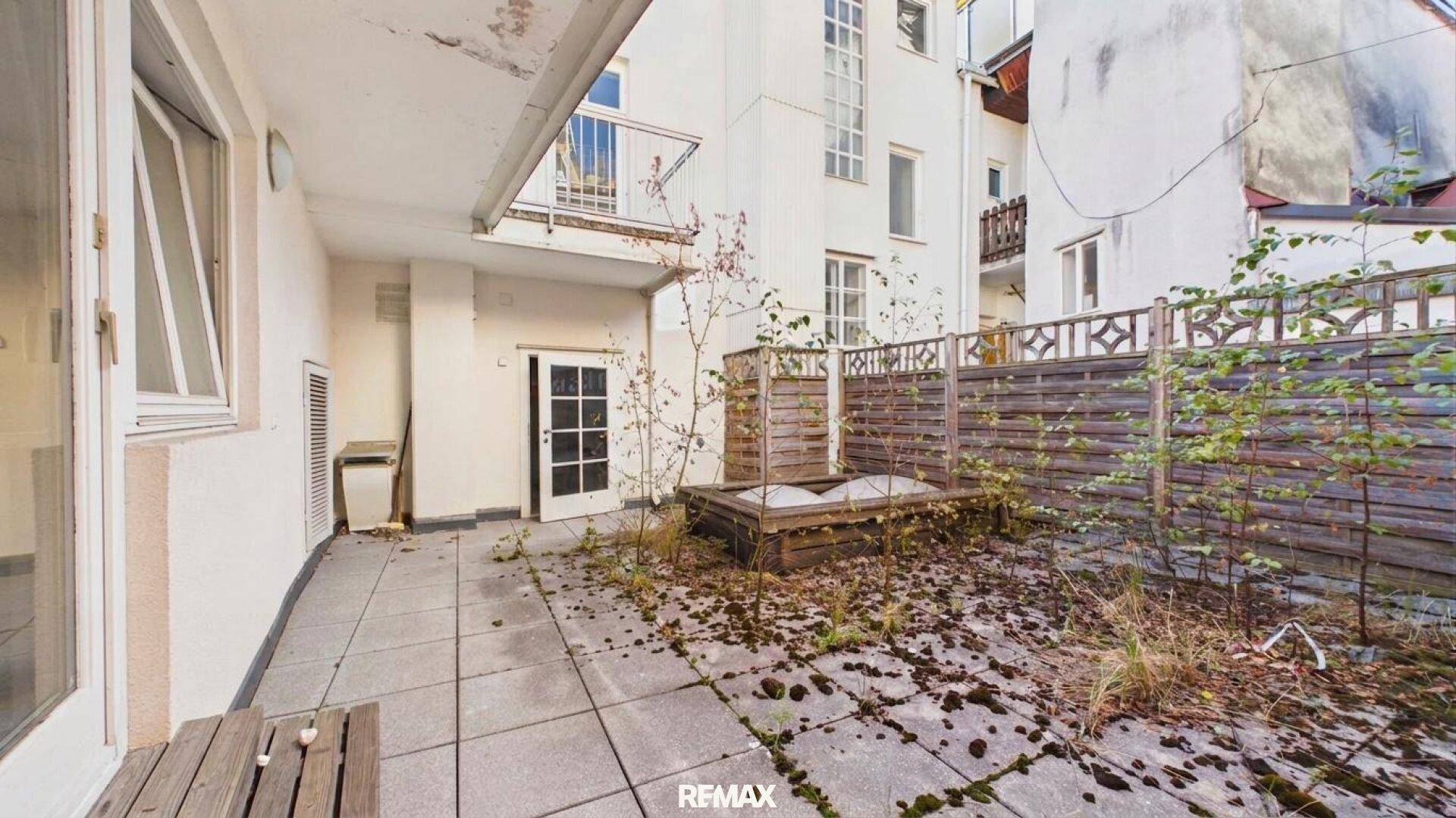 Außenbereich mit gepflasterter Terrasse, Holzzaun und Zugangstür zum Gebäude.