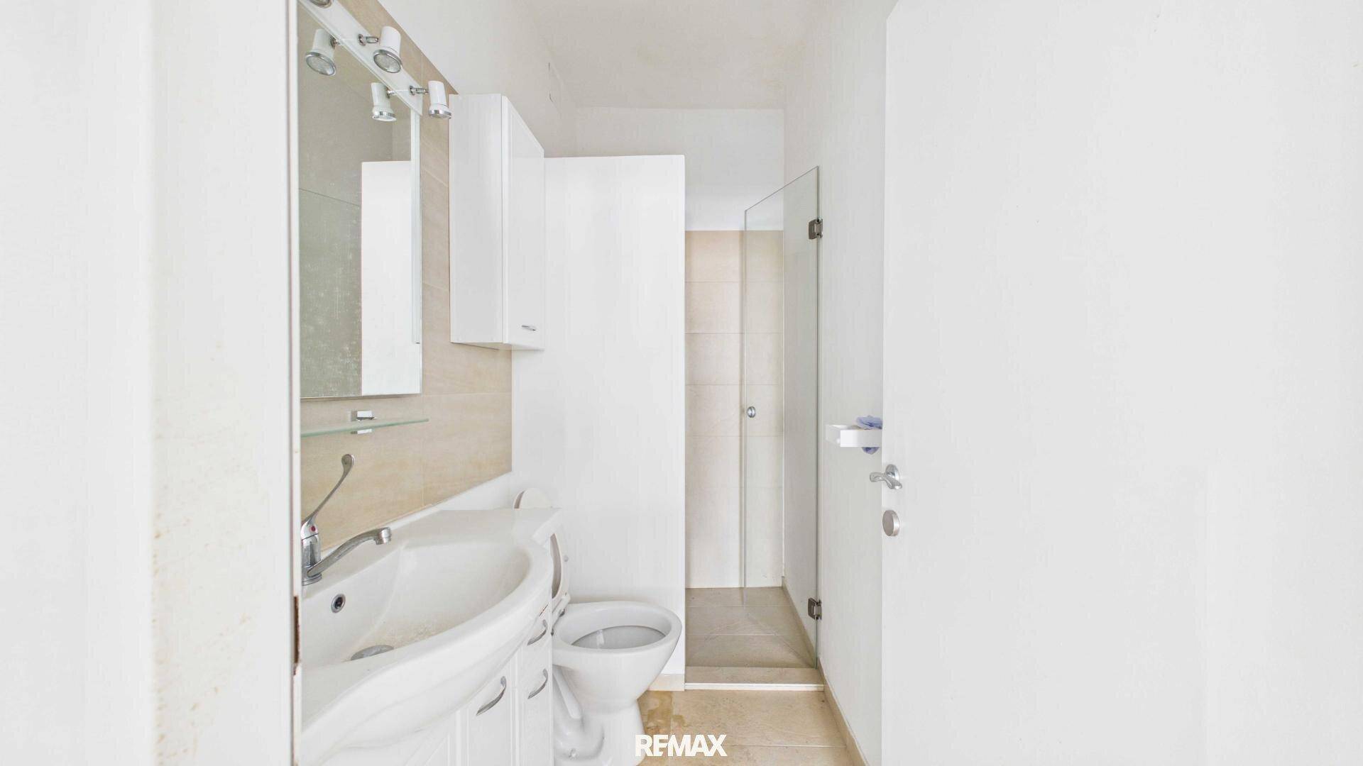 Modernes Badezimmer mit WC, Waschbecken, Spiegelschrank und Duschkabine.