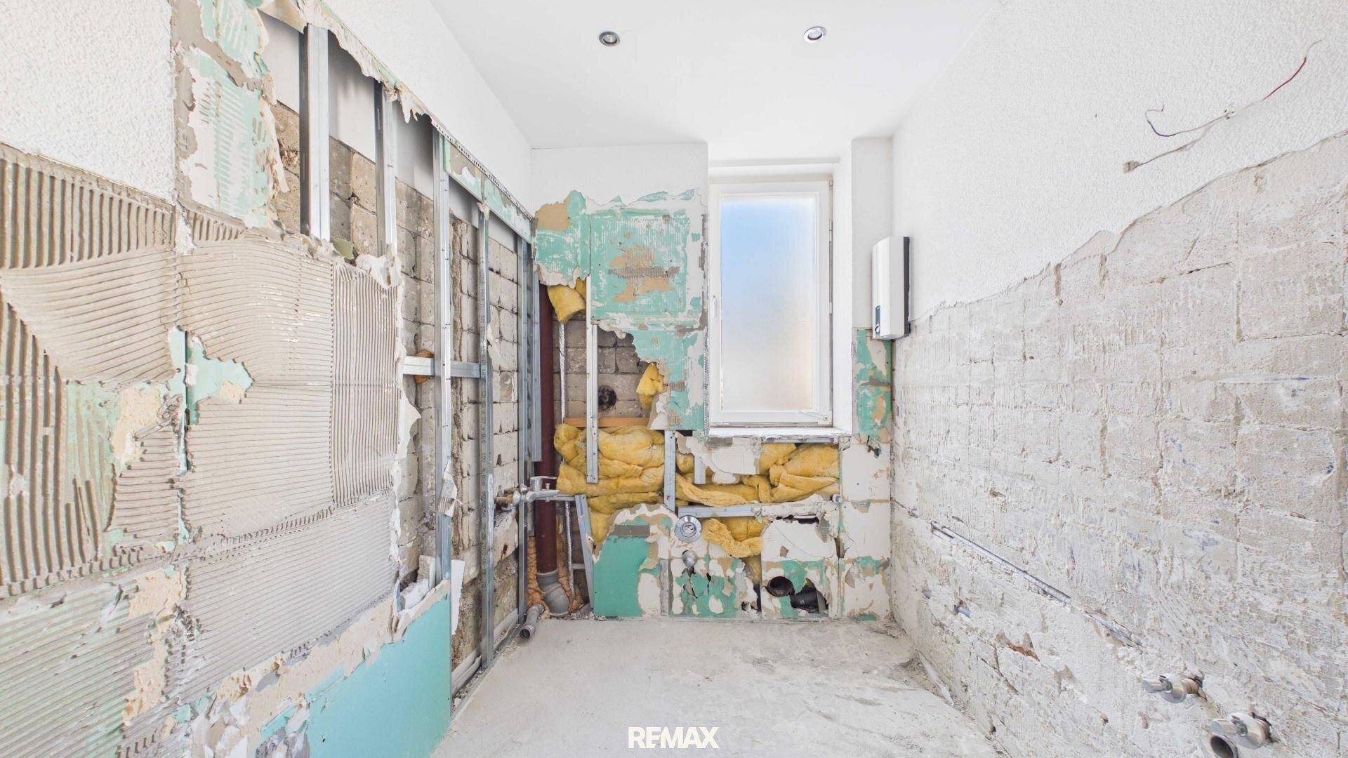 Badezimmer in fortgeschrittener Renovierung mit freigelegten Wänden und Installationen.