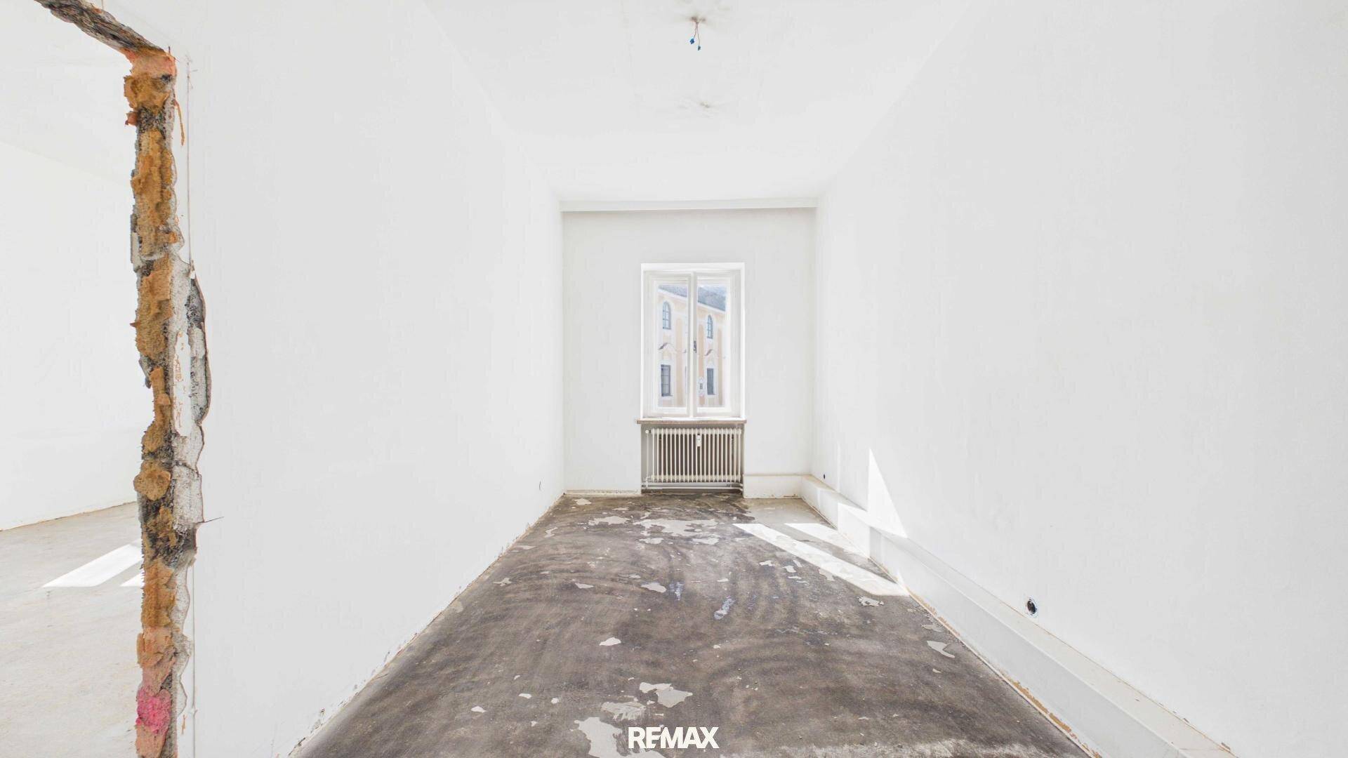 Leerer Raum in Renovierung mit weiß gestrichenen Wänden und einem Fenster.