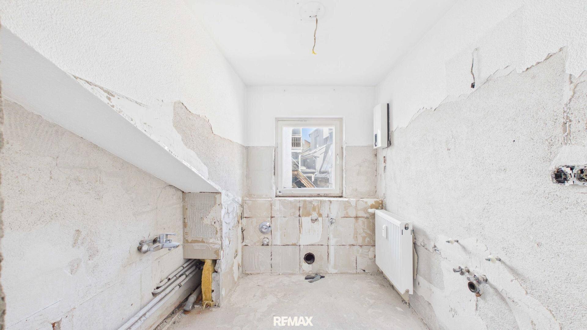 Renovierungsbedürftige Küche mit Fenster, Heizkörper und sichtbaren Installationen.