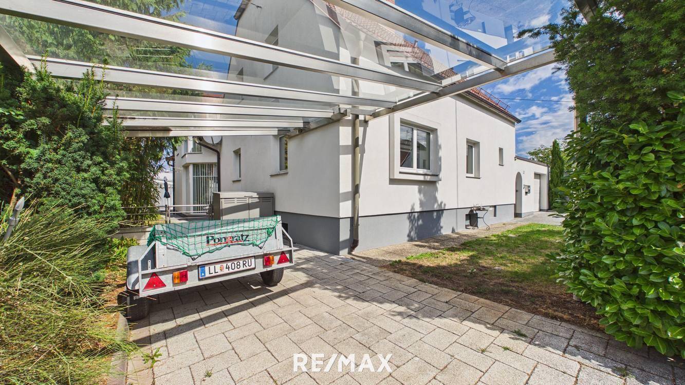 Überdachter Stellplatz (Carport) neben dem Haus mit gepflasterter Einfahrt.