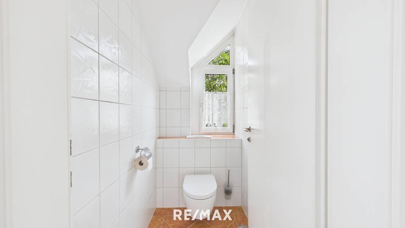 Separates WC mit weiß gefliesten Wänden und kleinem Fenster für natürliche Belüftung.