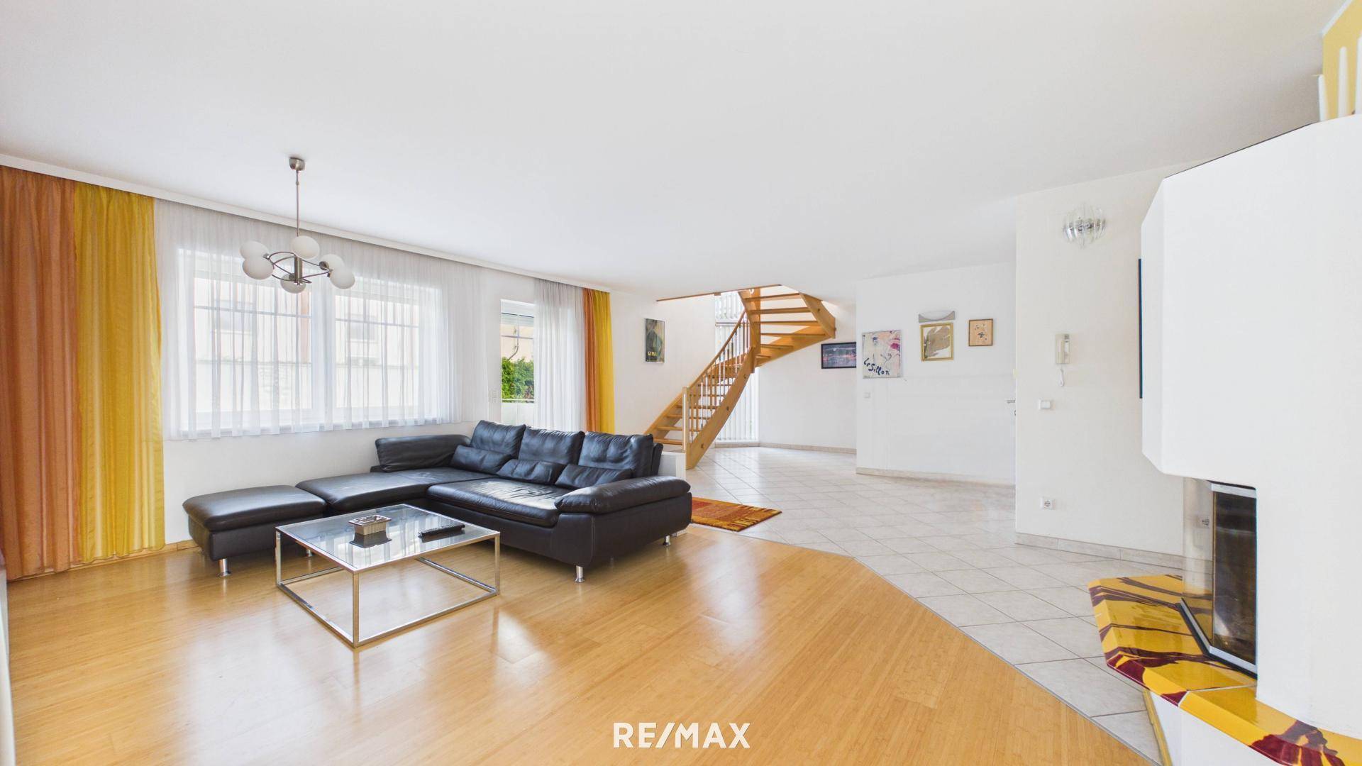 Helles Wohnzimmer mit Parkettboden, großer Couch und offener Treppe zum Obergeschoss.