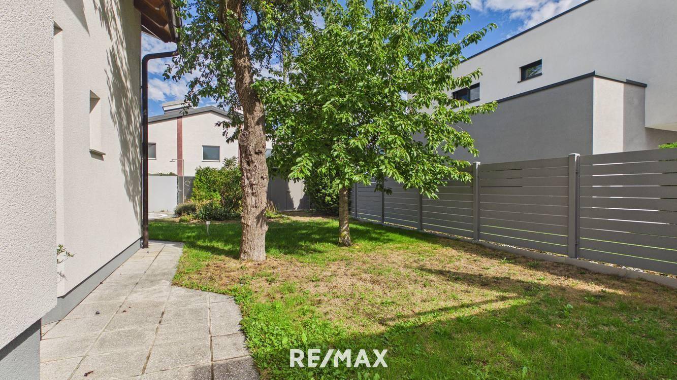 Seitlicher Gartenbereich mit Rasenfläche, jungen Bäumen und einem modernen Sichtschutzzaun.