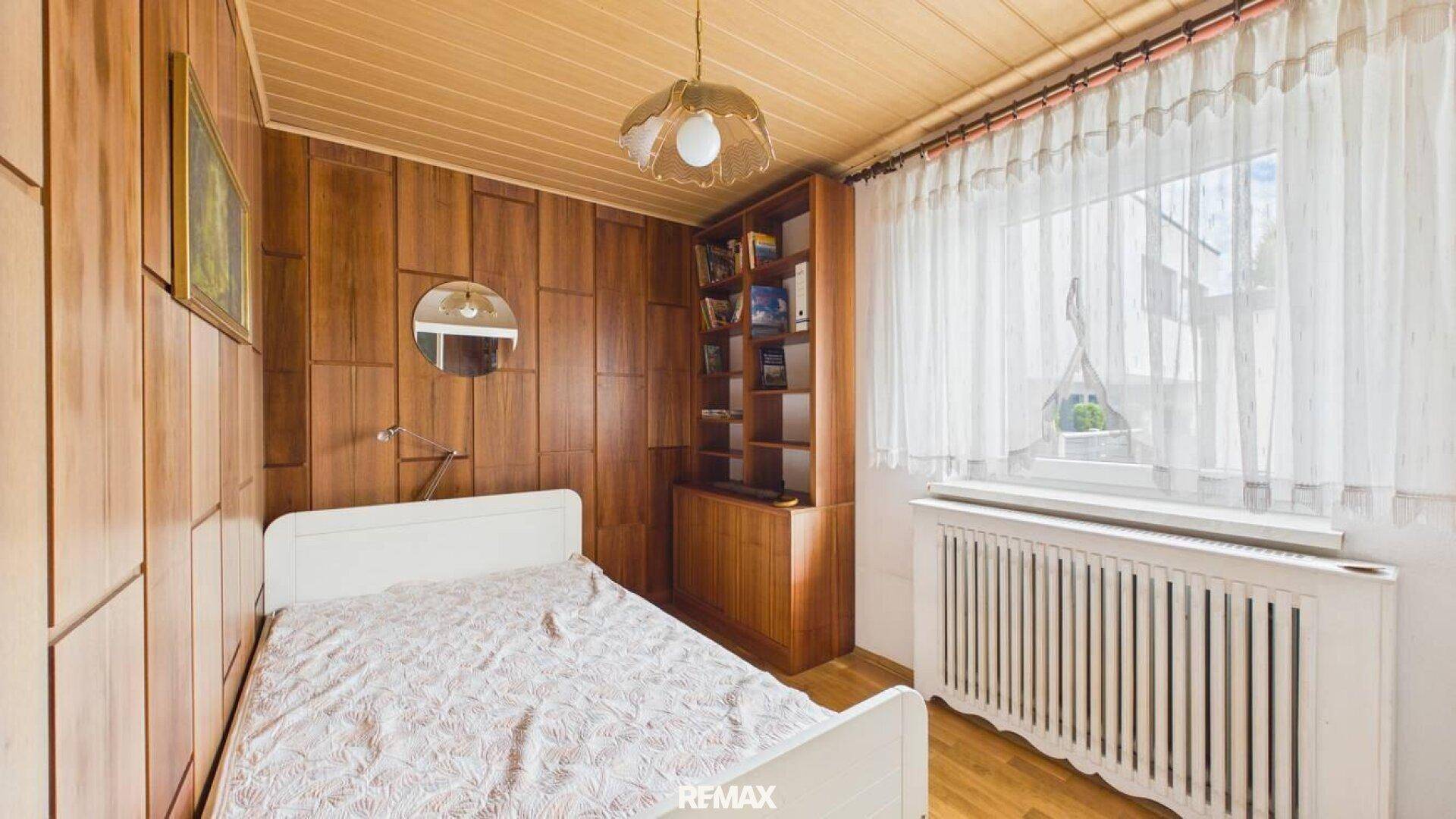 Schlafzimmer mit Holztäfelung, Einzelbett und Fenster, bietet eine warme Atmosphäre.