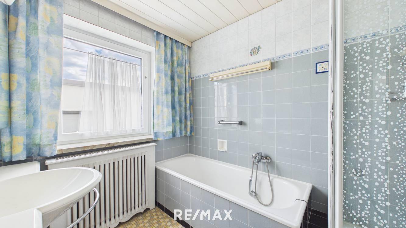 Badezimmer im 80er-Jahre-Stil mit Badewanne, Dusche und hellblauen Fliesen.