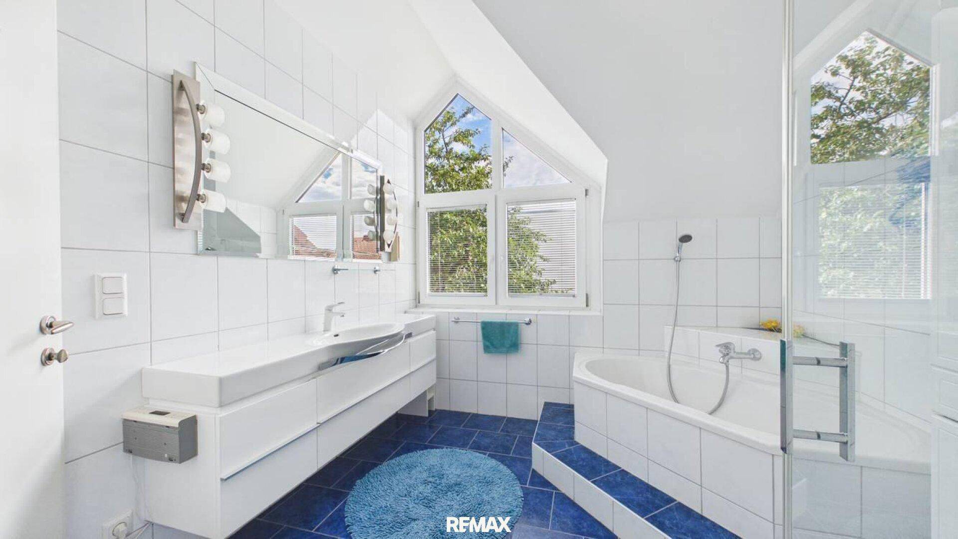 Modernes Badezimmer mit blauen Bodenfliesen, Badewanne und Dusche unter Dachschräge.
