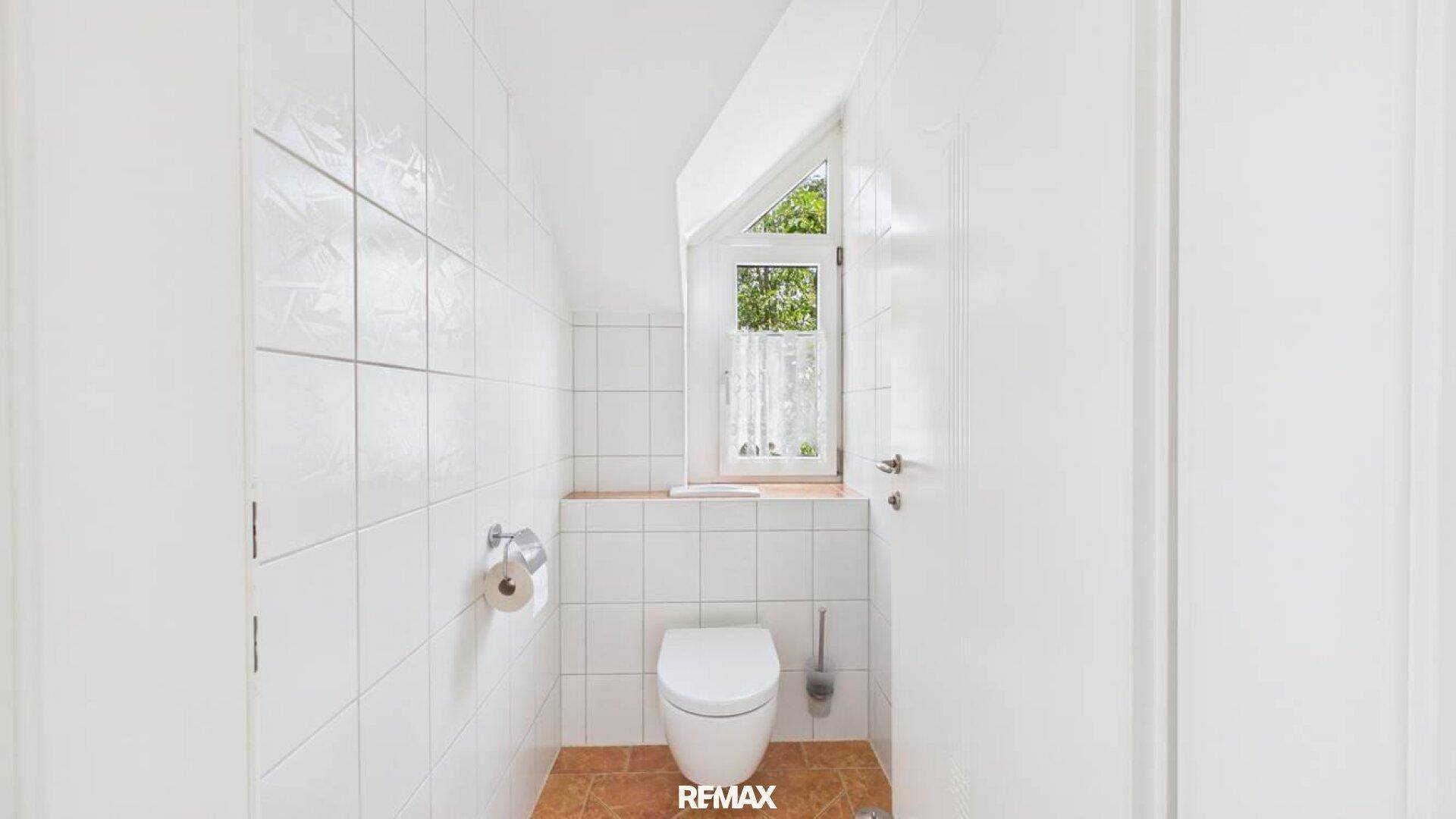 Separates WC mit weißen Wandfliesen und kleinem Fenster.