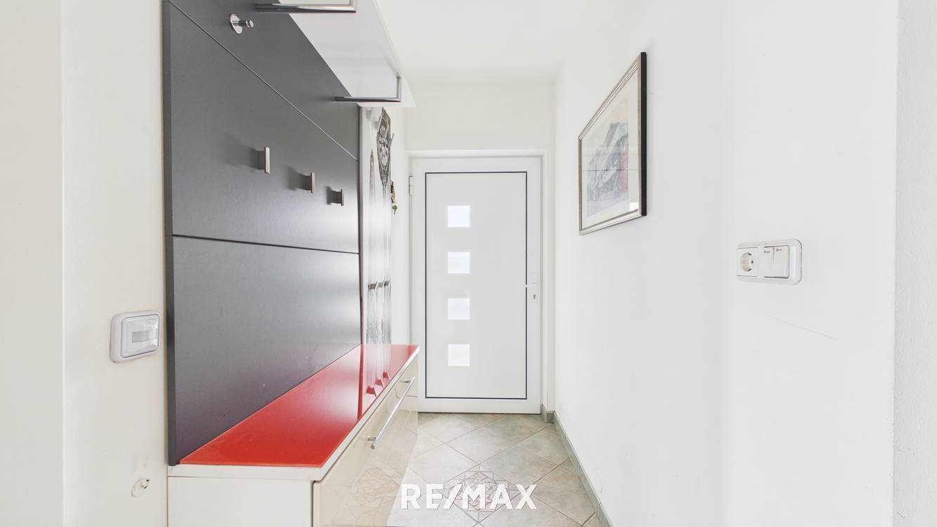 Heller Eingangsbereich mit Garderobe, Fliesenboden und moderner Haustür.