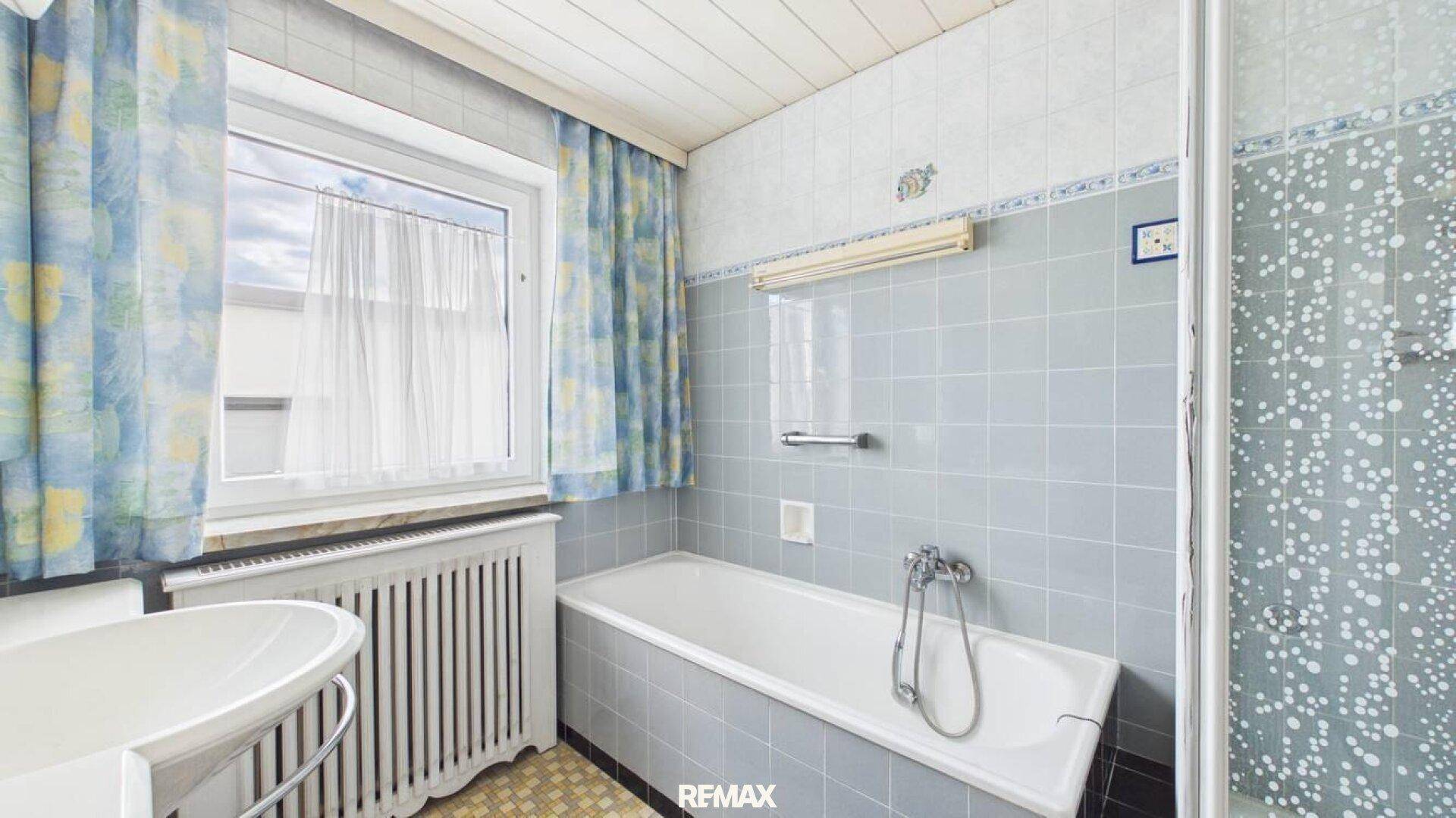 Badezimmer im Stil der 80er Jahre mit blauen Fliesen, Badewanne und Fenster.
