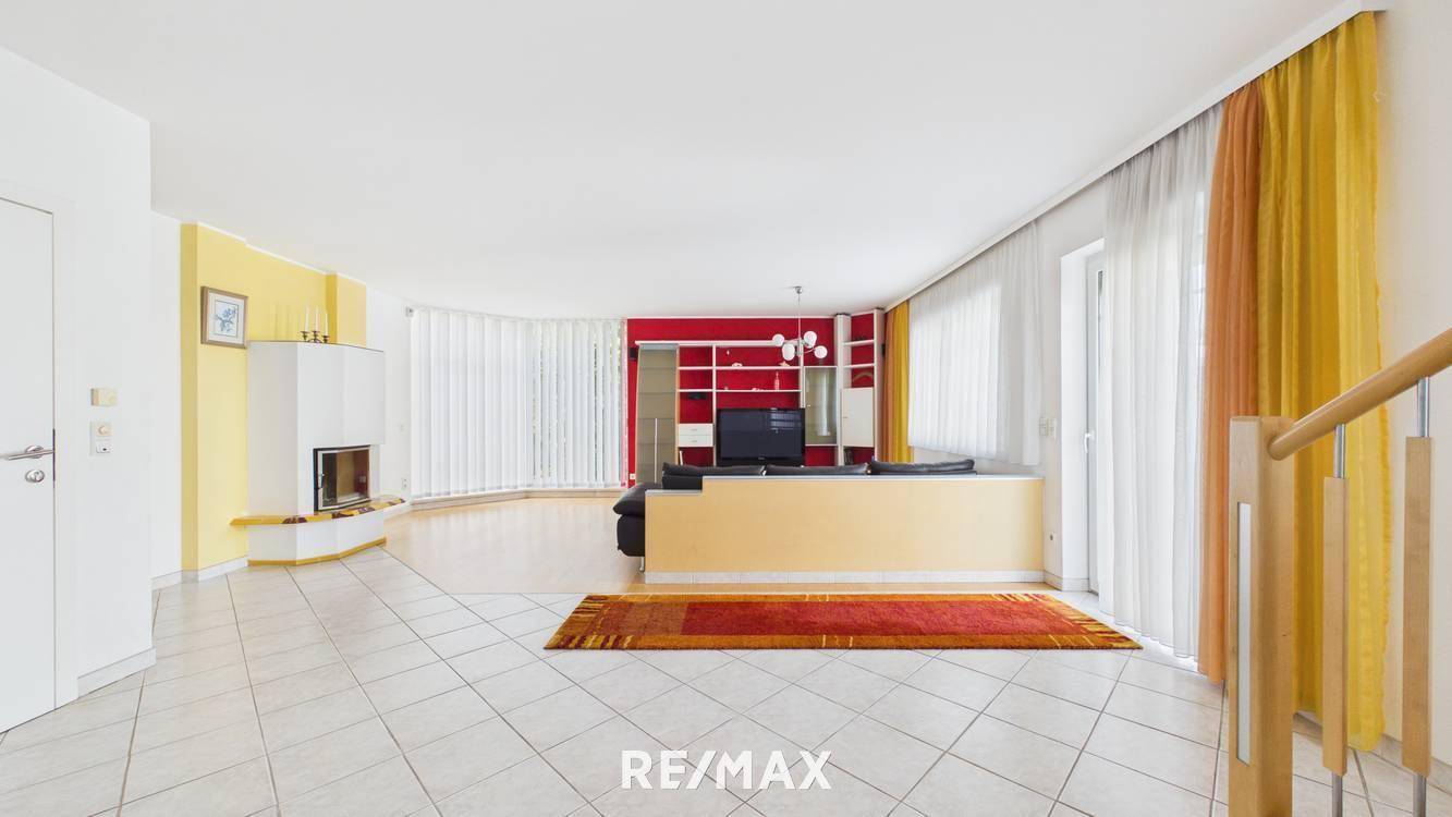 Geräumiges Wohnzimmer mit Kamin, Fliesenboden und farbenfroher Wandgestaltung in Rot und Gelb.