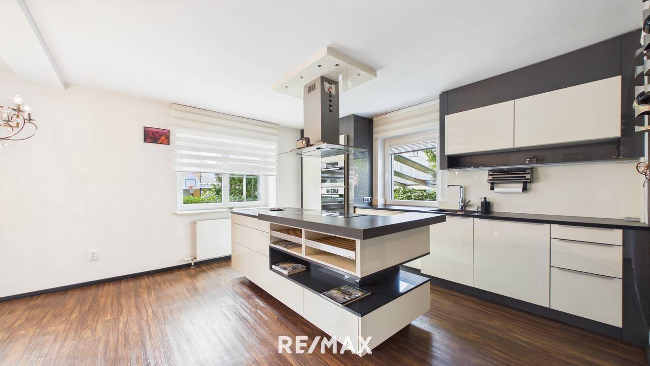 Moderne Küche mit Kücheninsel, dunklen Arbeitsplatten und integrierten Geräten.