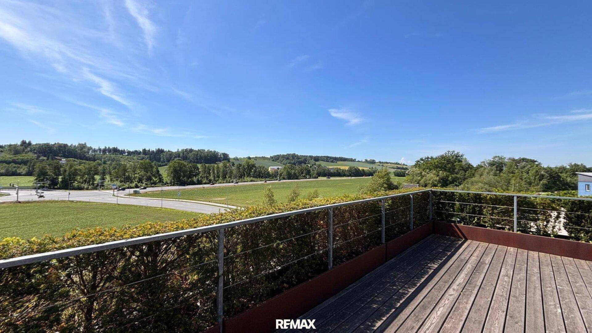 Weitläufige Holzterrasse mit Panoramablick auf die grüne Landschaft und den blauen Himmel.