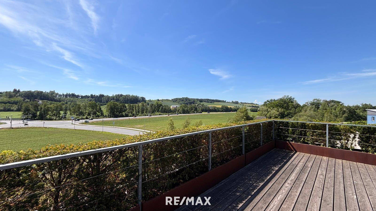 Große Holzterrasse mit weitem Blick über die grüne Landschaft und den blauen Himmel.