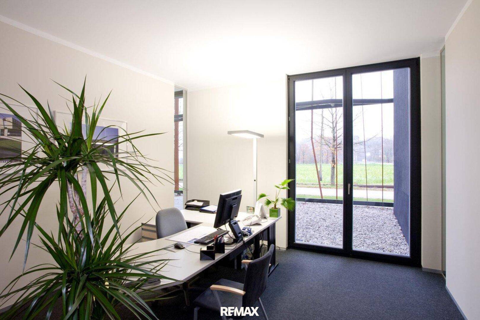 Helles Büro mit großem Fenster, Blick ins Grüne und modernem Schreibtisch.