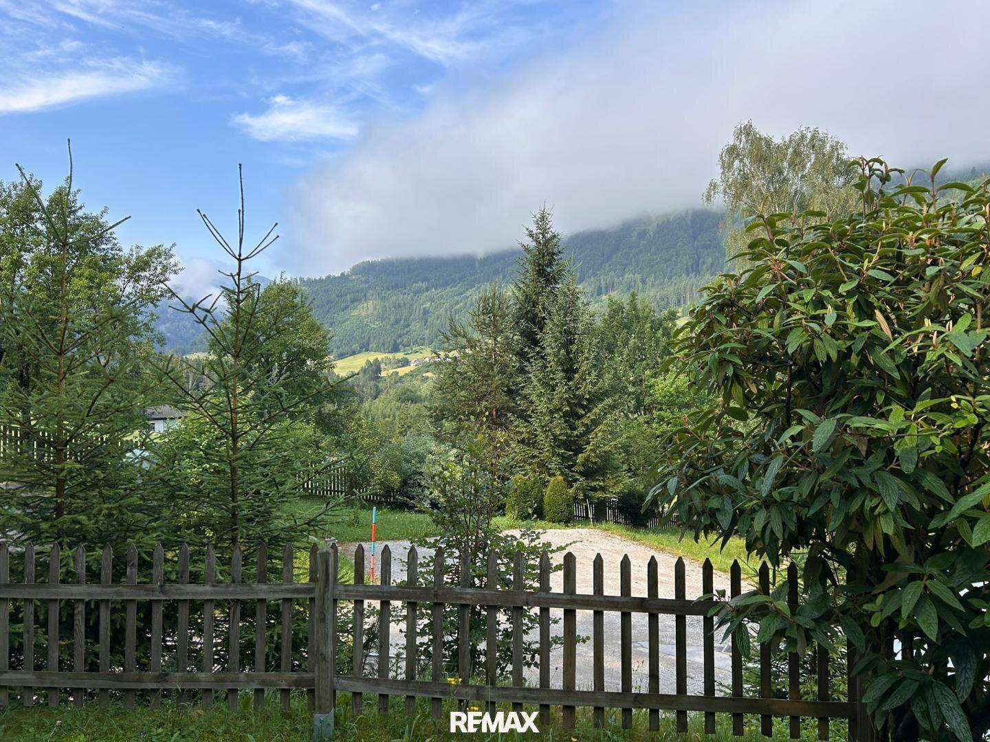 Weitläufiger Blick über grüne Hügel und Wälder mit einem Holzzaun im Vordergrund.