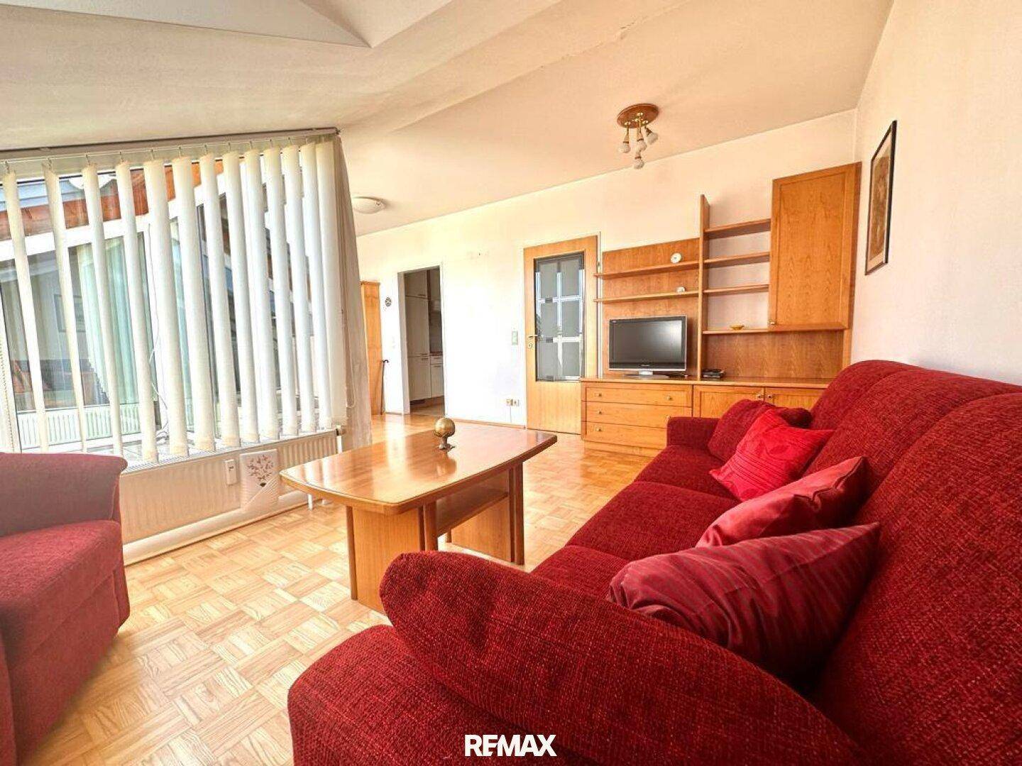 Gemütliches Wohnzimmer mit rotem Sofa, Holztisch und Parkettboden.