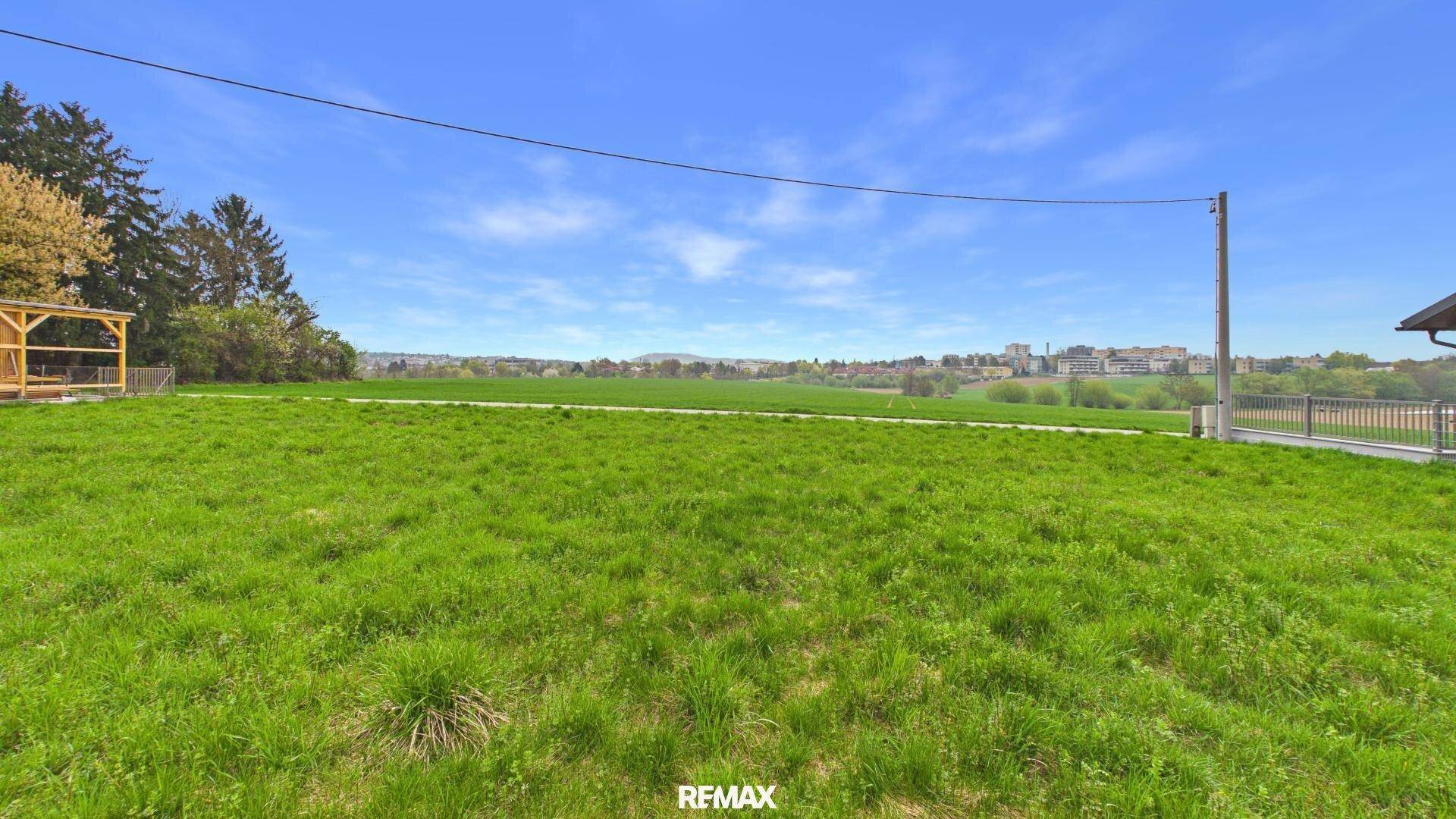Offenes grünes Grundstück mit Blick auf die umliegende Landschaft und entfernte Bebauung.