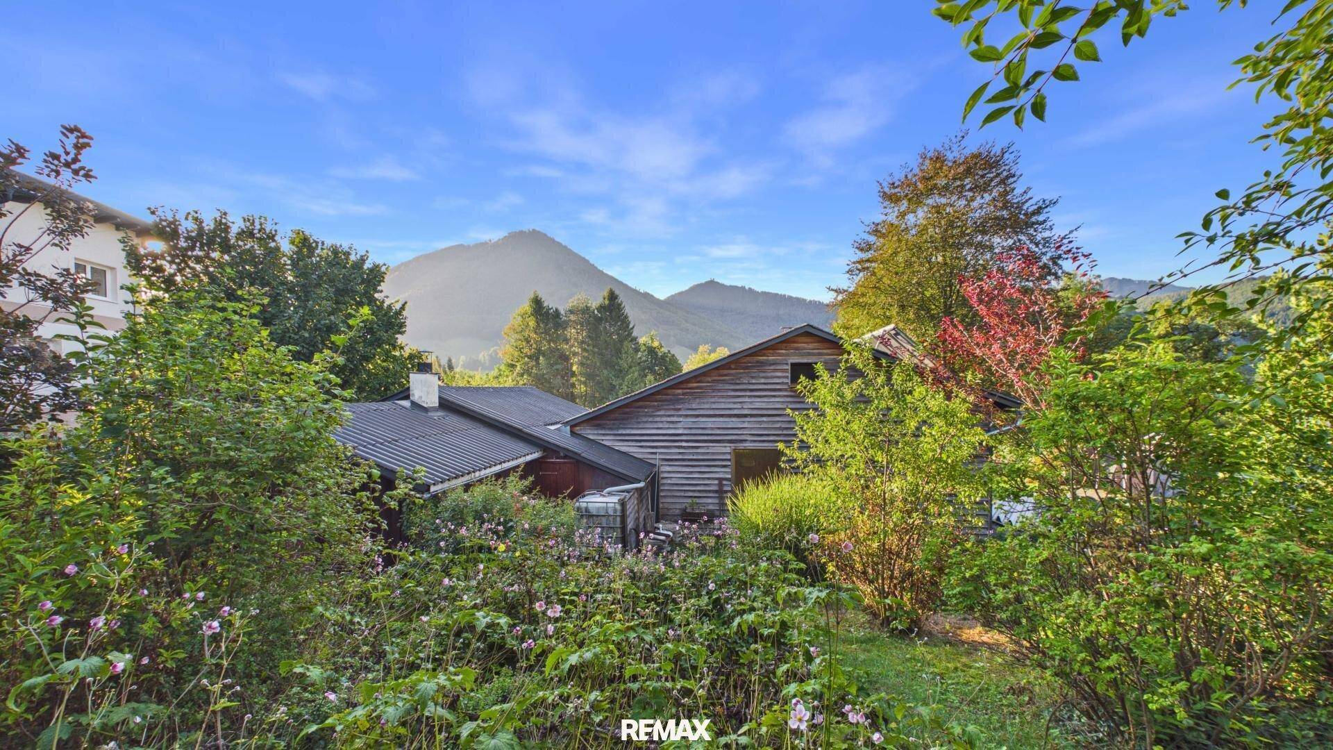 Hausfassade aus Holz inmitten einer grünen Landschaft mit Bergen im Hintergrund.