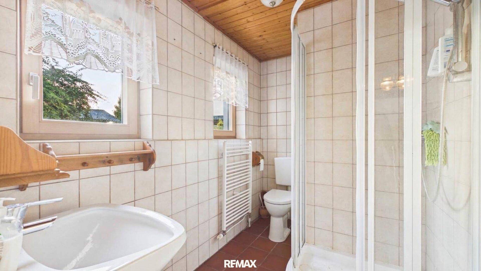 Badezimmer mit Dusche, Waschbecken, WC und hellen Fliesen an den Wänden.