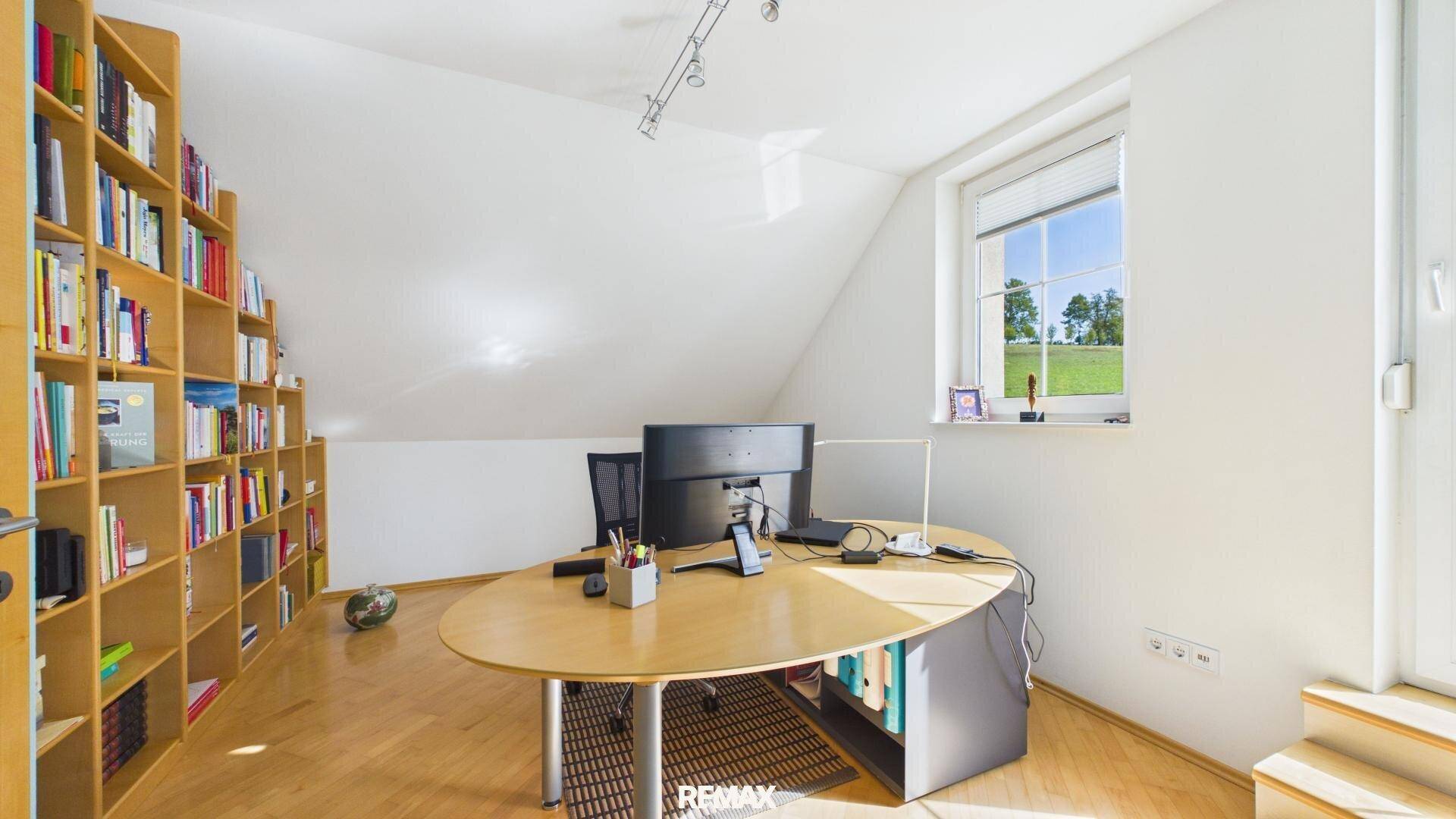 Helles Arbeitszimmer mit großem Bücherregal, Schreibtisch und Blick ins Grüne.