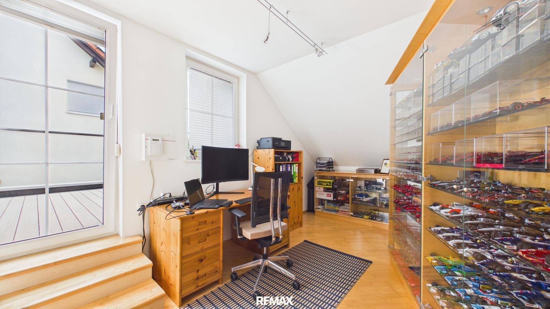 Arbeits- oder Hobbyzimmer mit Schreibtisch, Vitrinen und Zugang zu einem weiteren Bereich.