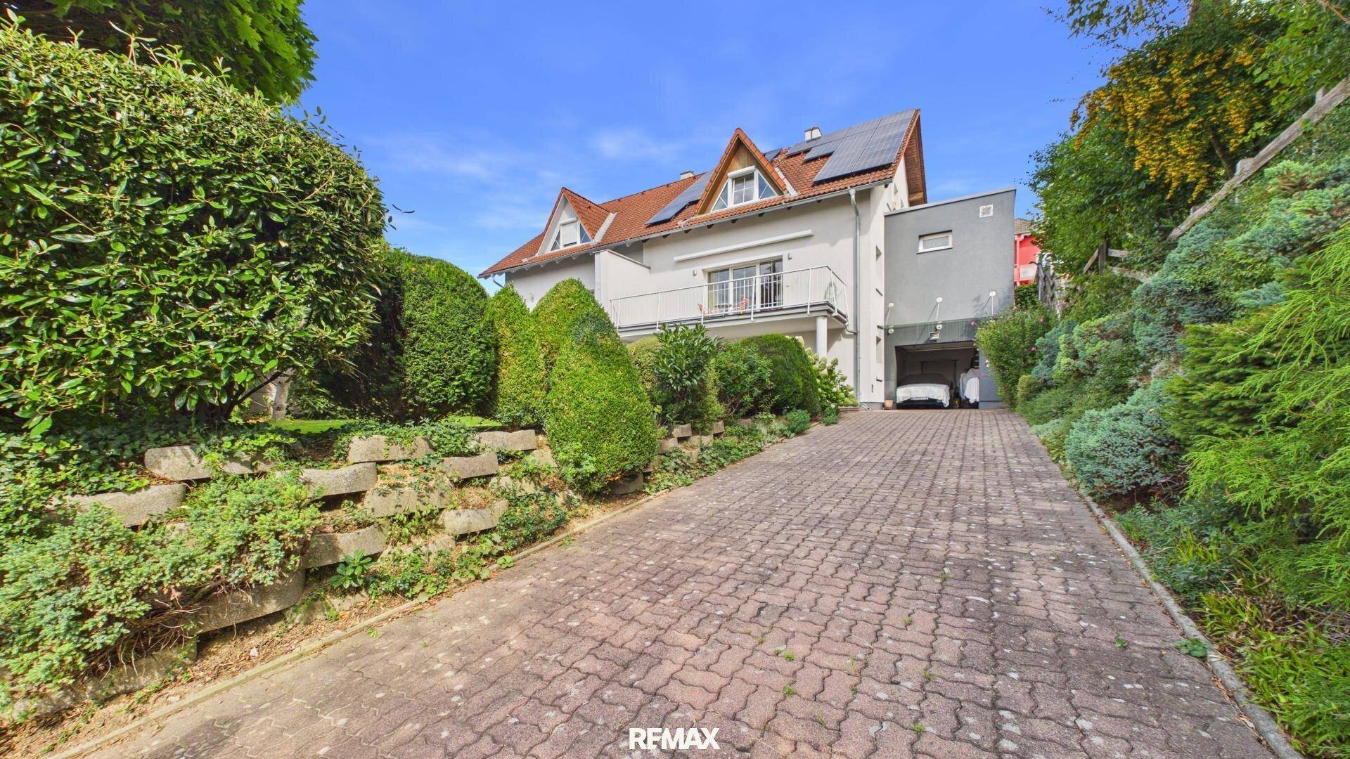 Einfamilienhaus mit gepflasterter Auffahrt, umgeben von üppigem Grün und Bäumen.