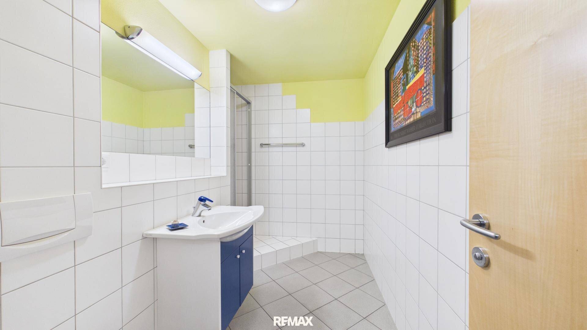 Funktionales Badezimmer mit weißen Fliesen, Dusche und Einzelwaschbecken.