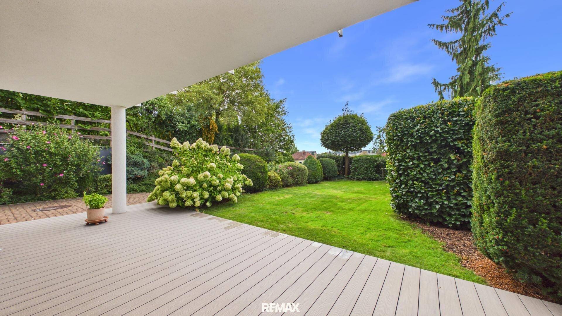 Geräumige überdachte Terrasse mit Holzdeck und Blick auf den gepflegten Garten.