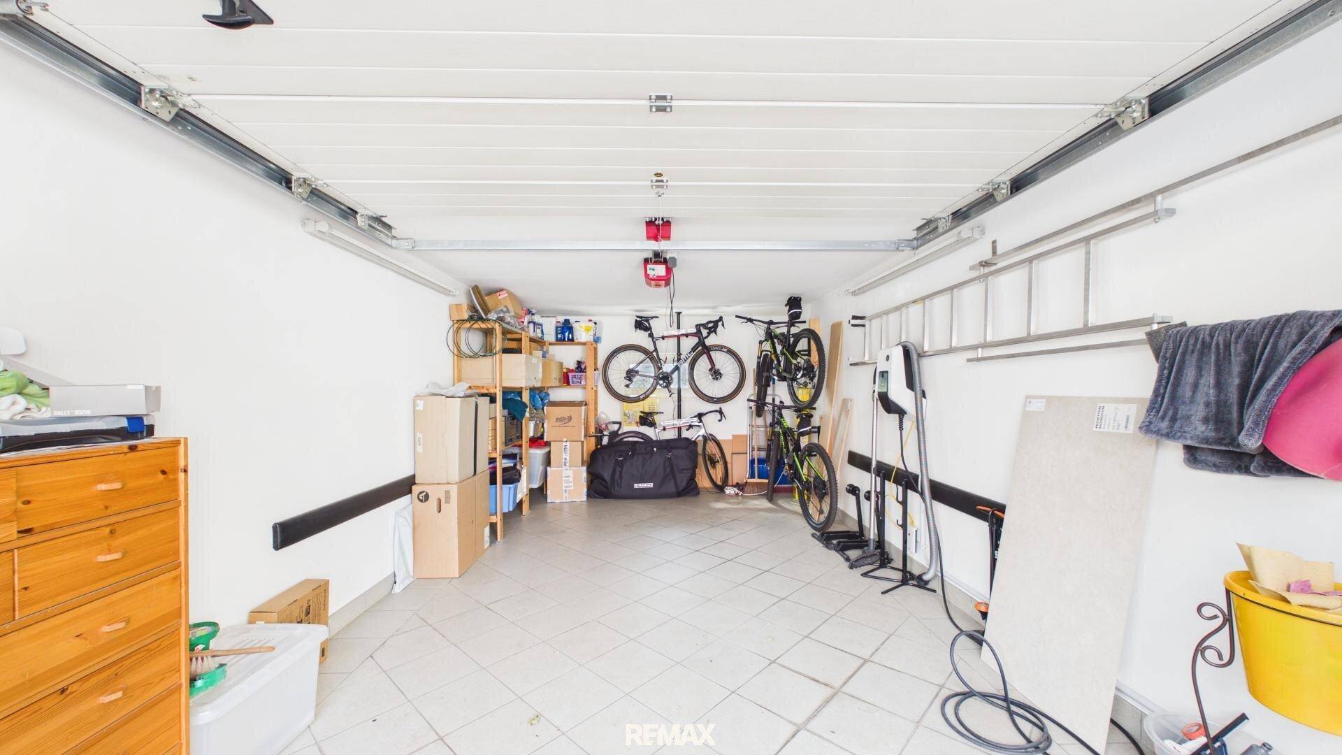 Geräumige Garage mit Fahrradaufhängungen, Regalen und einer Ladestation für Elektrofahrzeuge.