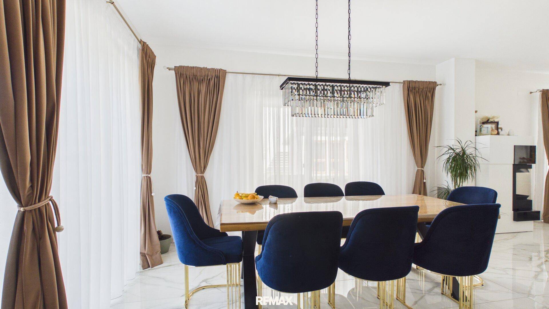 Eleganter Essbereich mit großem Holztisch, blauen Samtstühlen und Kronleuchter.