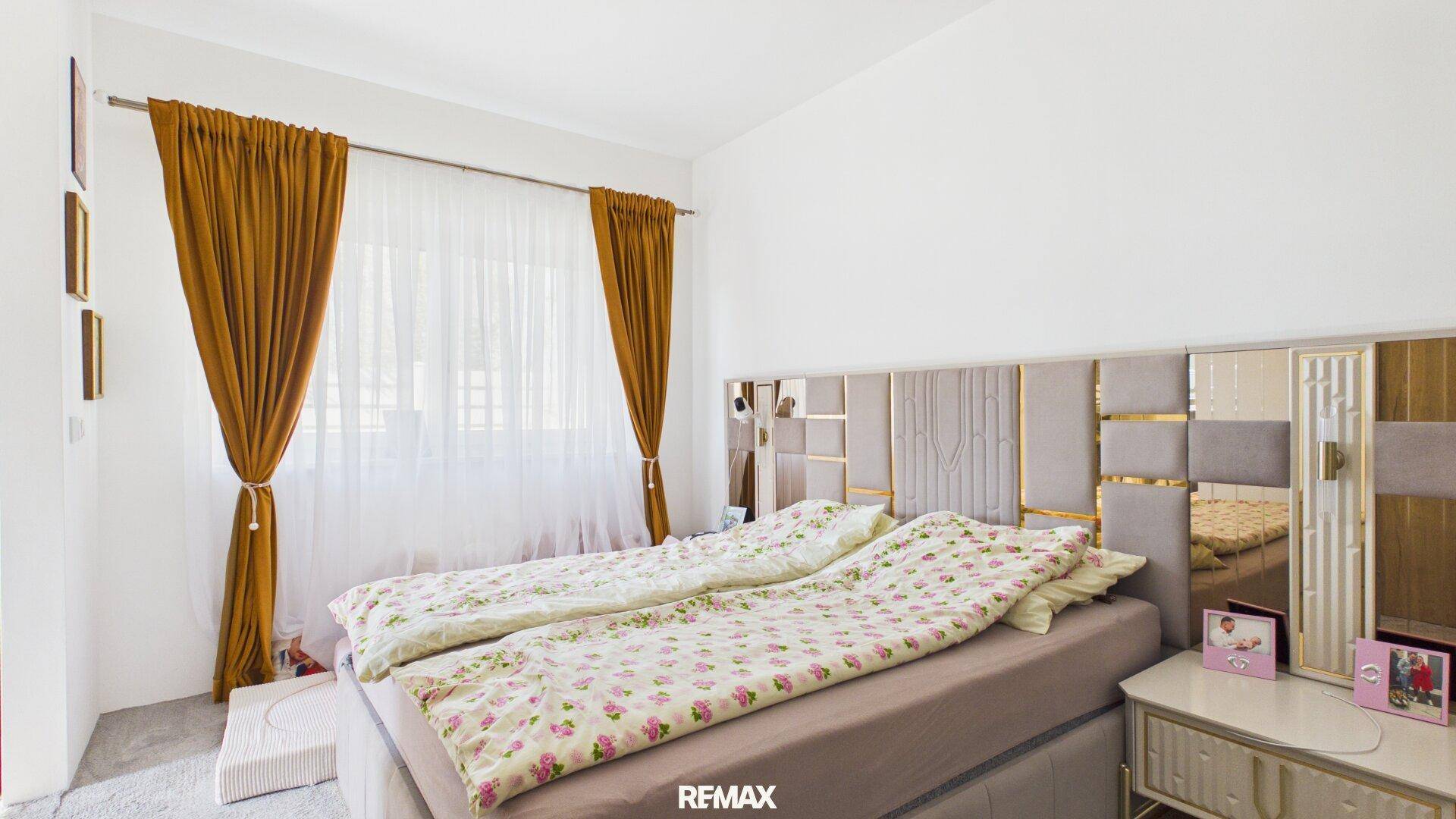Helles Schlafzimmer mit großem Bett, gepolstertem Kopfteil und braunen Vorhängen.