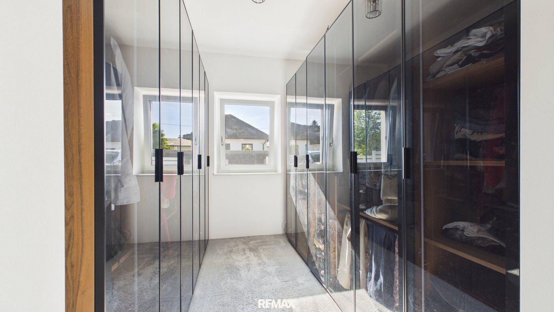 Geräumiger begehbarer Kleiderschrank mit modernen Glasfronten und viel Stauraum.