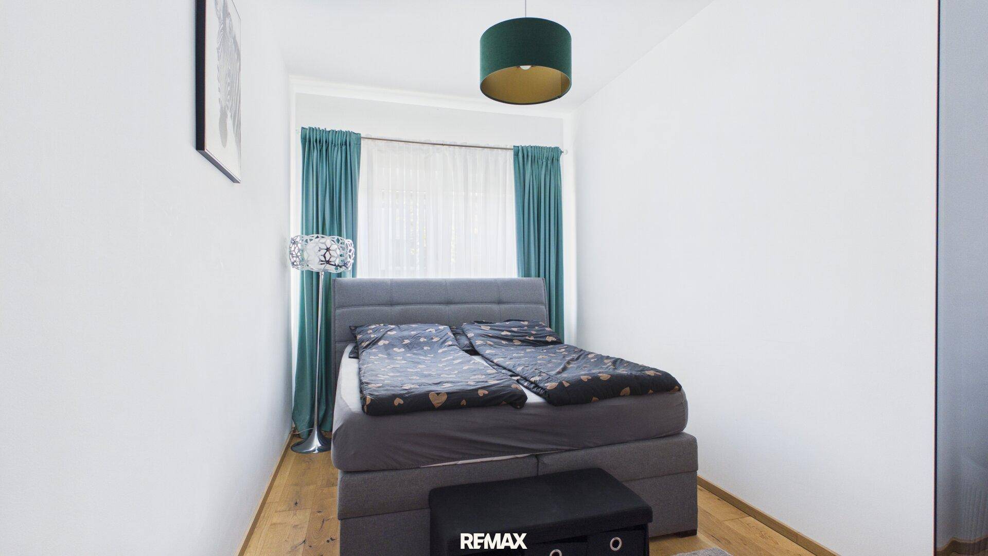 Gemütliches Schlafzimmer mit Boxspringbett, Holzboden und türkisfarbenen Vorhängen.