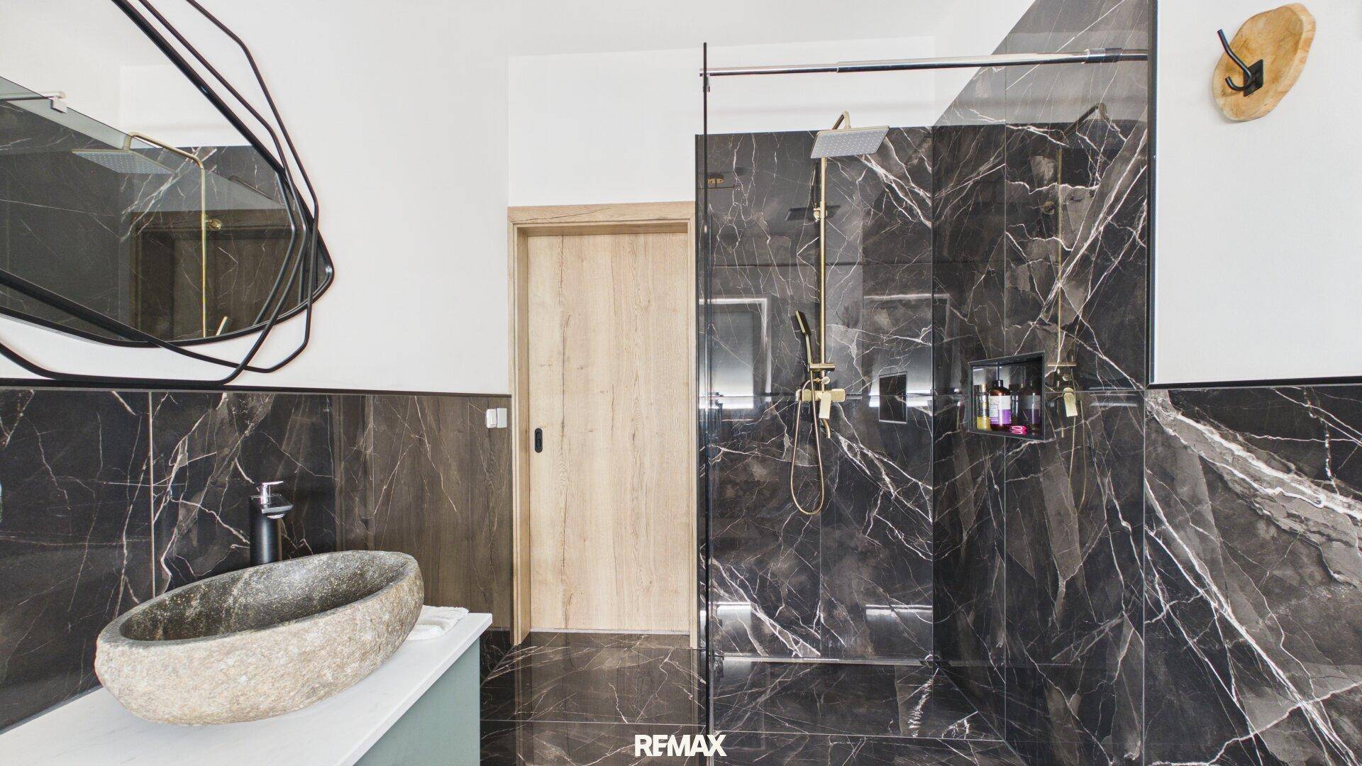 Luxuriöses Badezimmer mit dunklen Marmorfliesen, Steinsink und großer begehbarer Dusche.