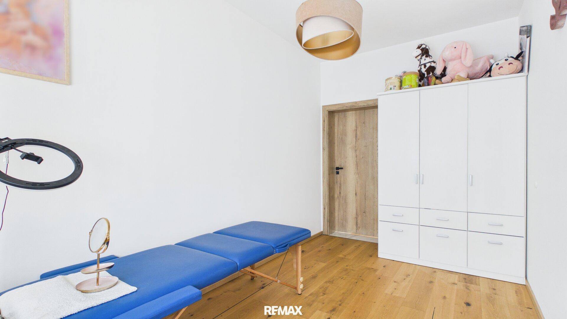 Heller Raum mit Holzboden, weißem Schrank und einer blauen Behandlungsliege.