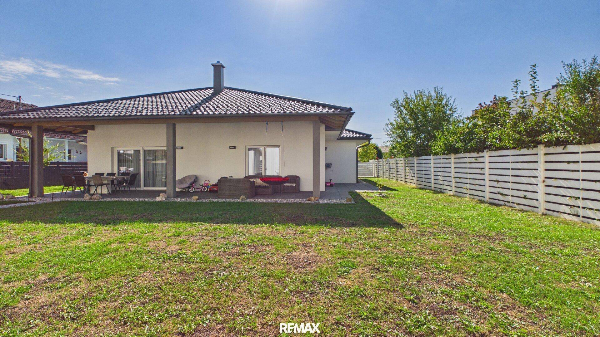 Großer, gepflegter Garten mit Rasenfläche und überdachter Terrasse mit Sitzgelegenheiten.
