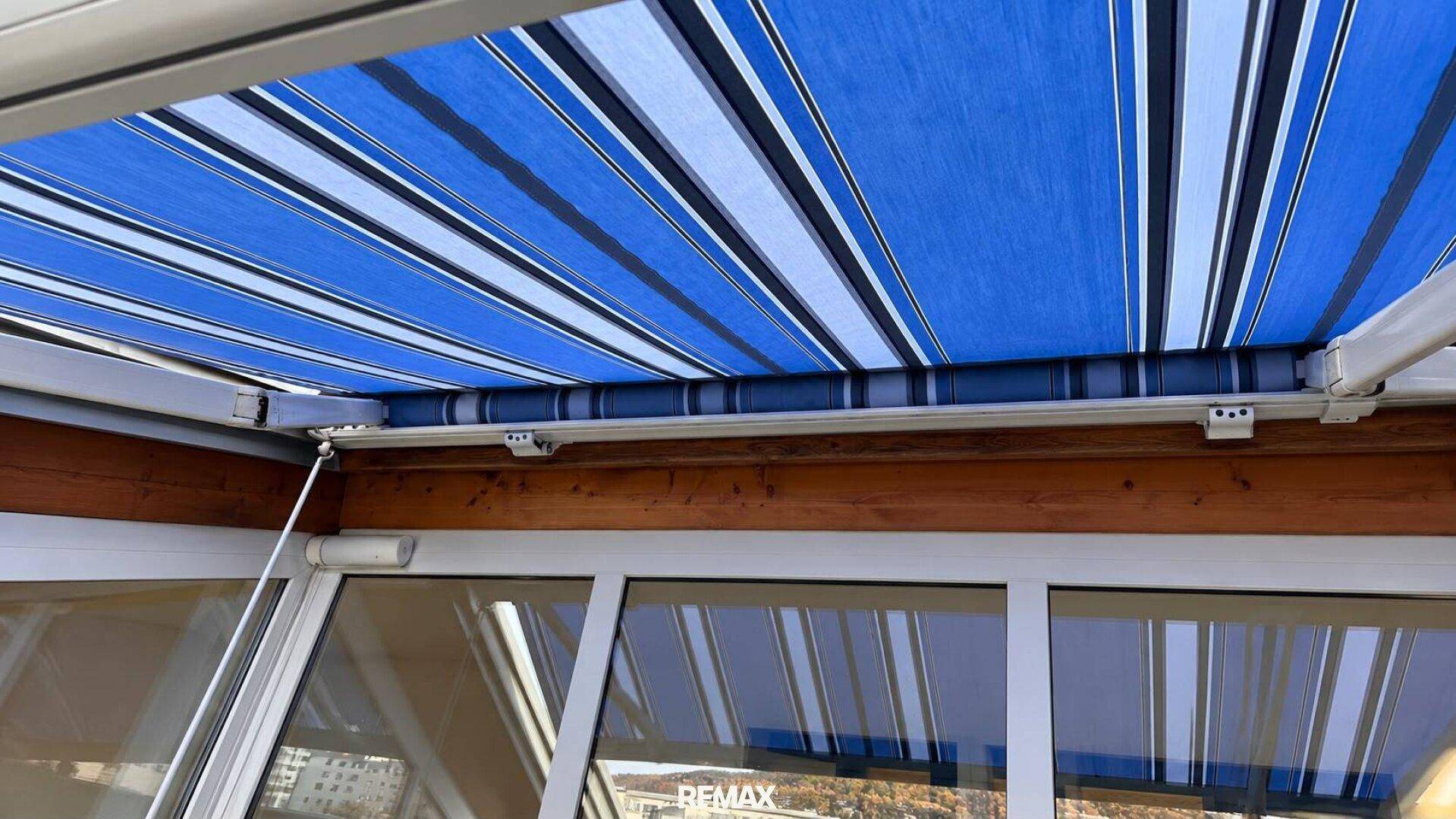 Blaue und weiße gestreifte Markise über den Fenstern, die Schatten spendet.