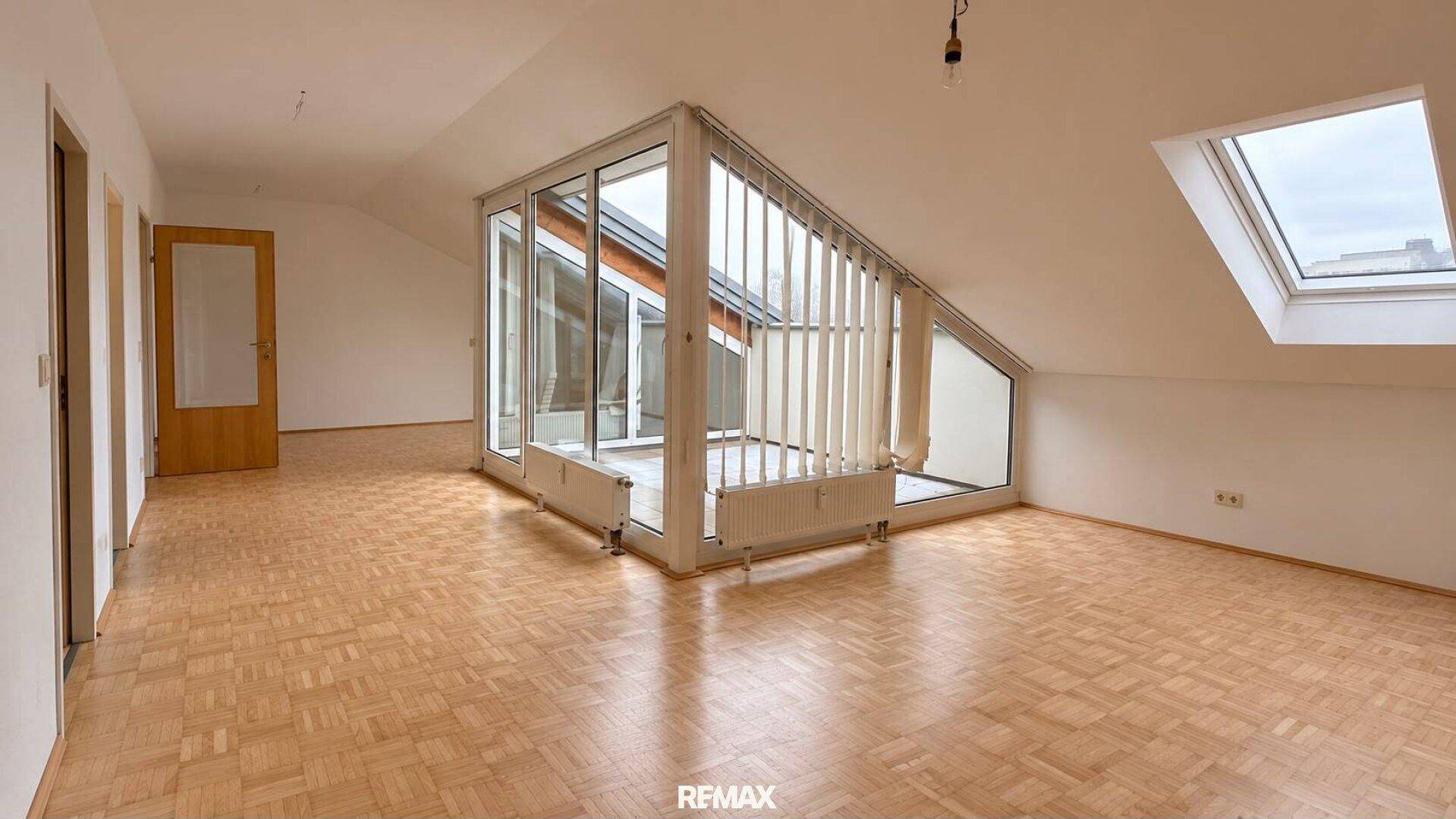 Geräumiger, unmöblierter Raum mit Parkettboden, Dachschrägen und großen Glasfronten.