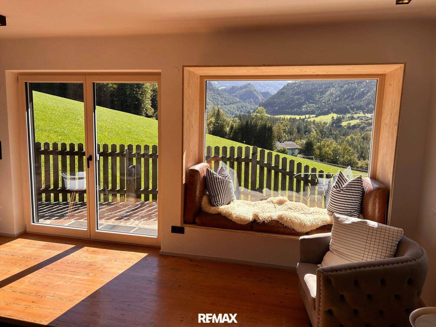 Helles Wohnzimmer mit gemütlicher Fensterbank und Panoramablick auf die Berge und das Tal.
