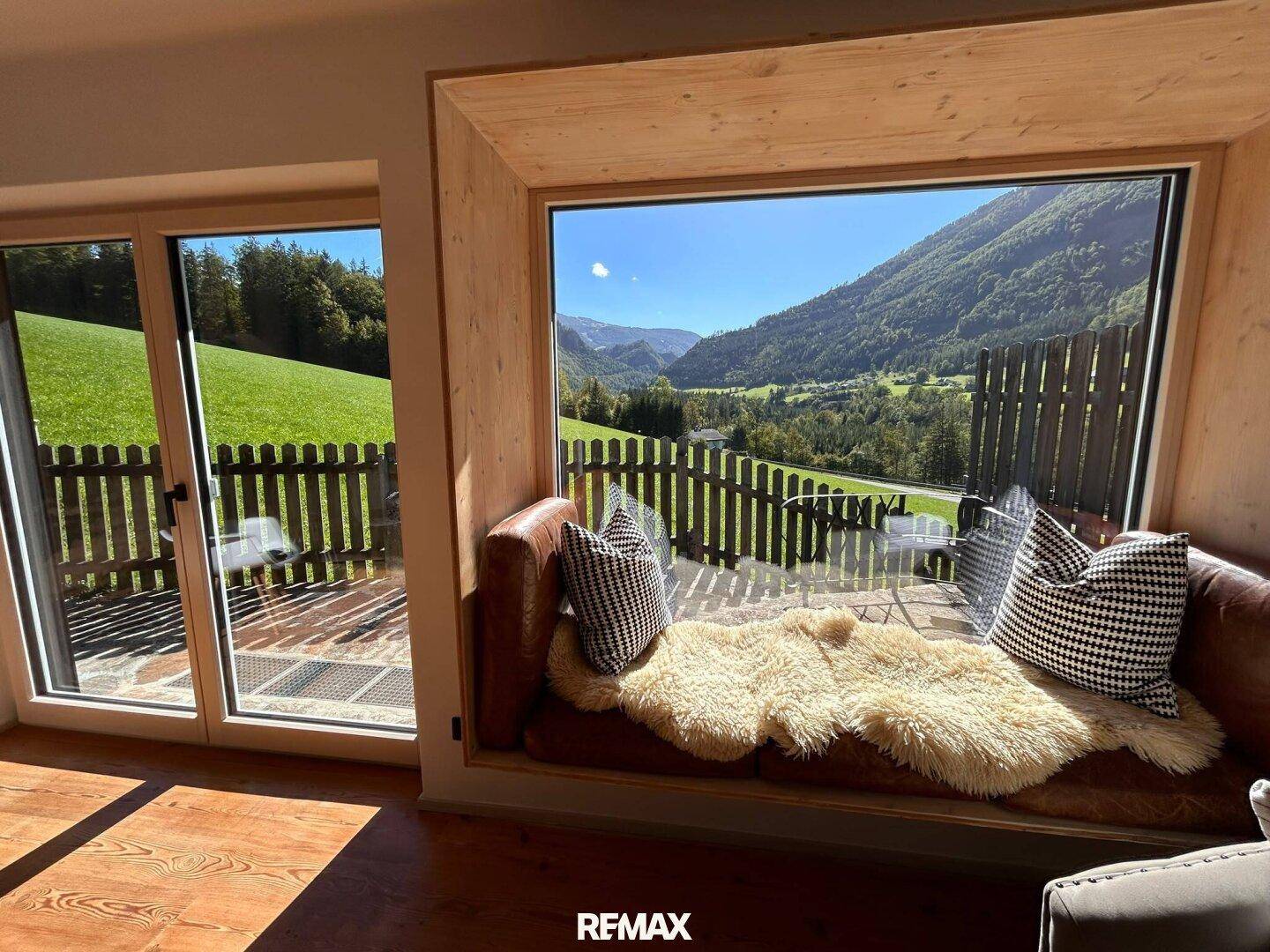 Gemütlicher Fensterplatz mit weitem Blick auf die Berge und grüne Täler, umrahmt von hellem Holz.