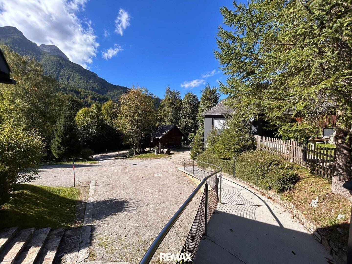Ein geschwungener Weg mit Metallgeländer führt zu einem Haus, umgeben von Schotterflächen und der beeindruckenden Berglandschaft.