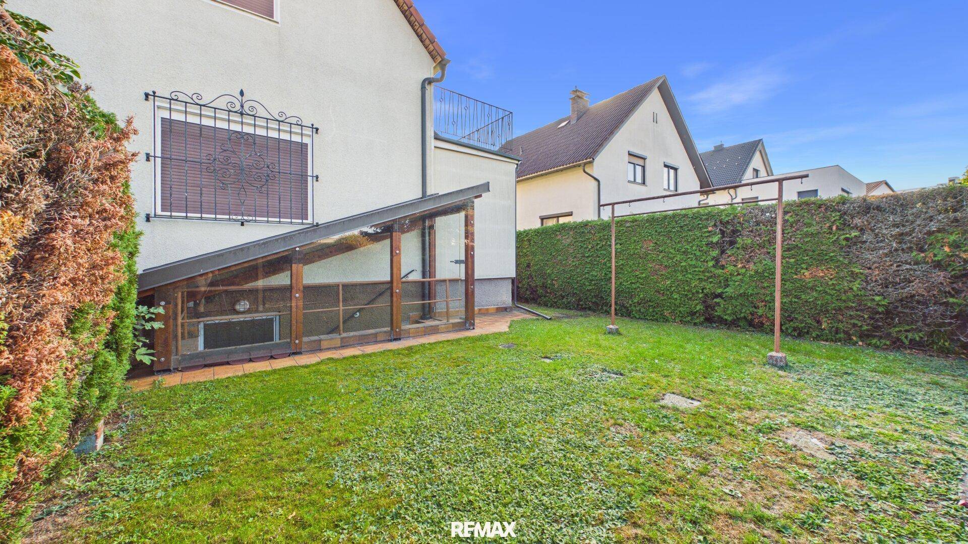 Seitlicher Gartenbereich mit Rasen, Hecke und einem kleinen Anbau, möglicherweise ein Gewächshaus.