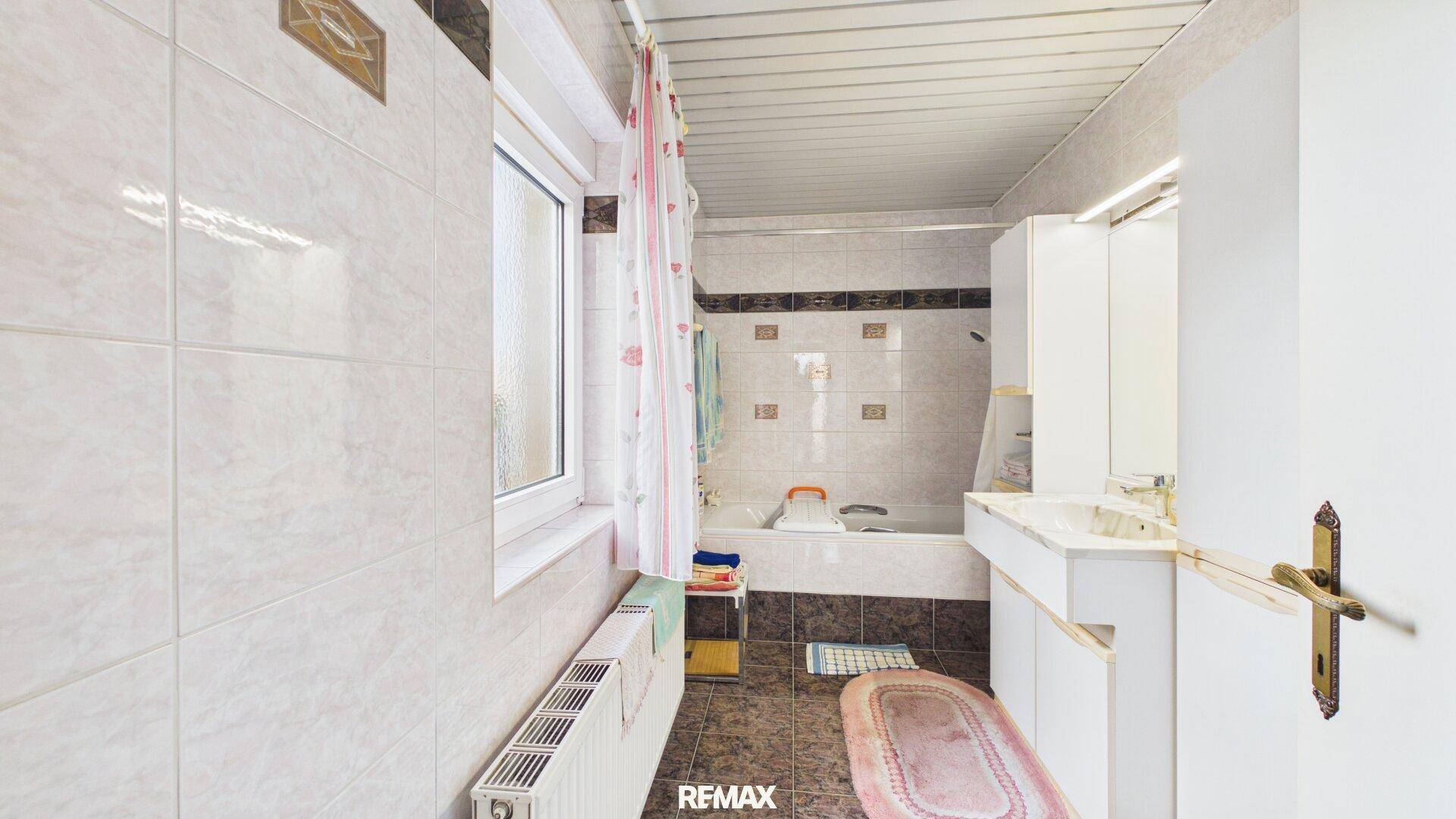 Helles Badezimmer mit Badewanne, Fenster und weißen Fliesen im traditionellen Stil.