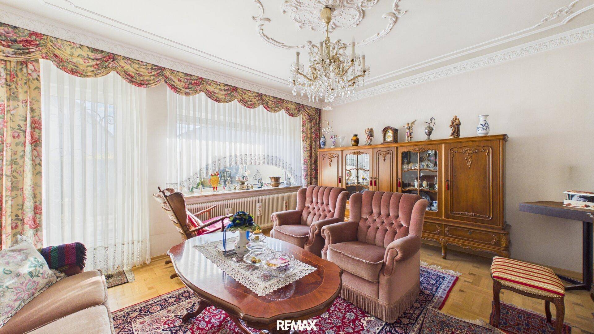 Elegantes Wohnzimmer mit Stuckdecke, Kronleuchter und klassischen Polstermöbeln in Rosa.