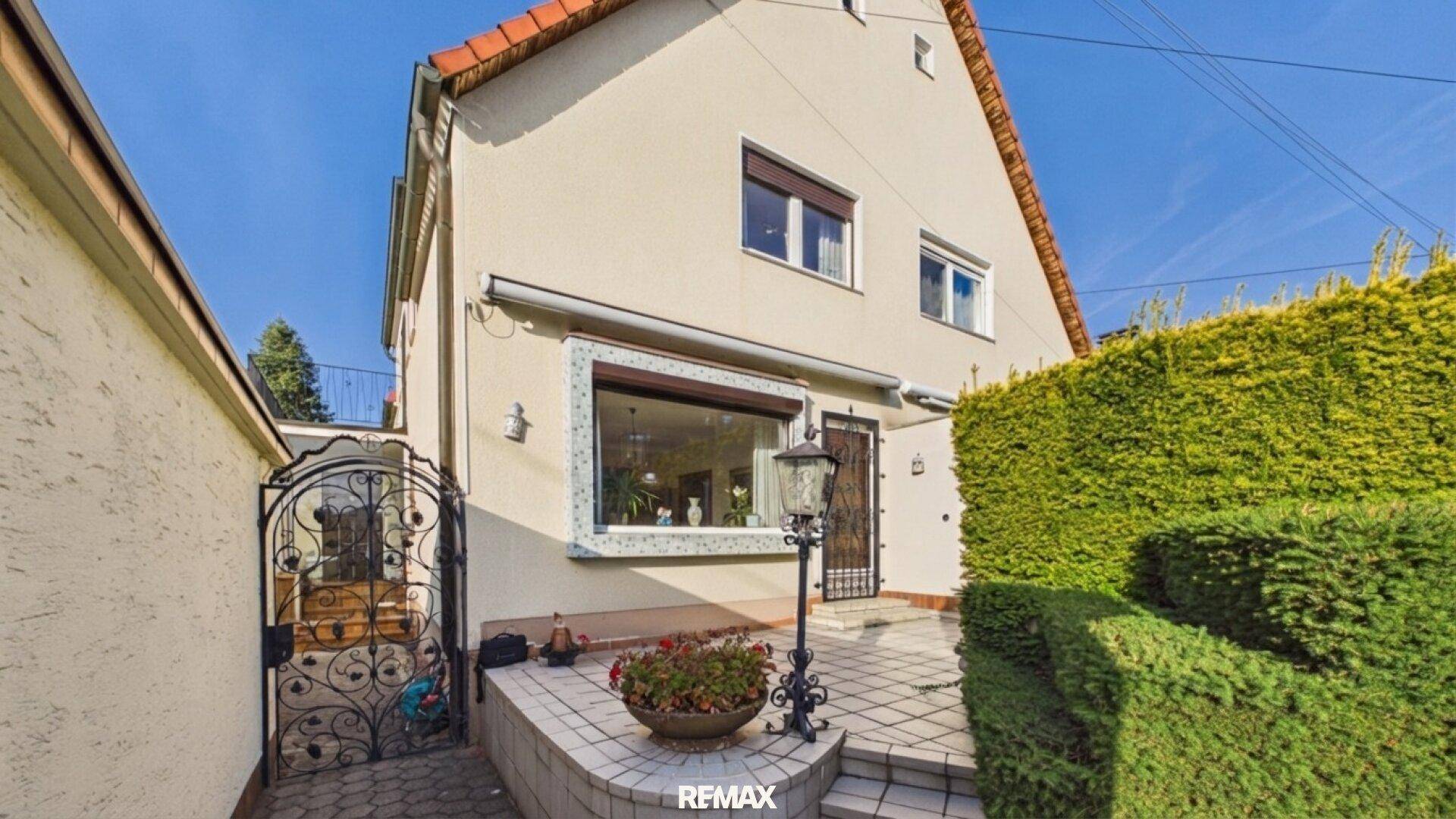 Seitlicher Eingangsbereich mit gefliester Terrasse, dekorativer Laterne und gepflegter Hecke.