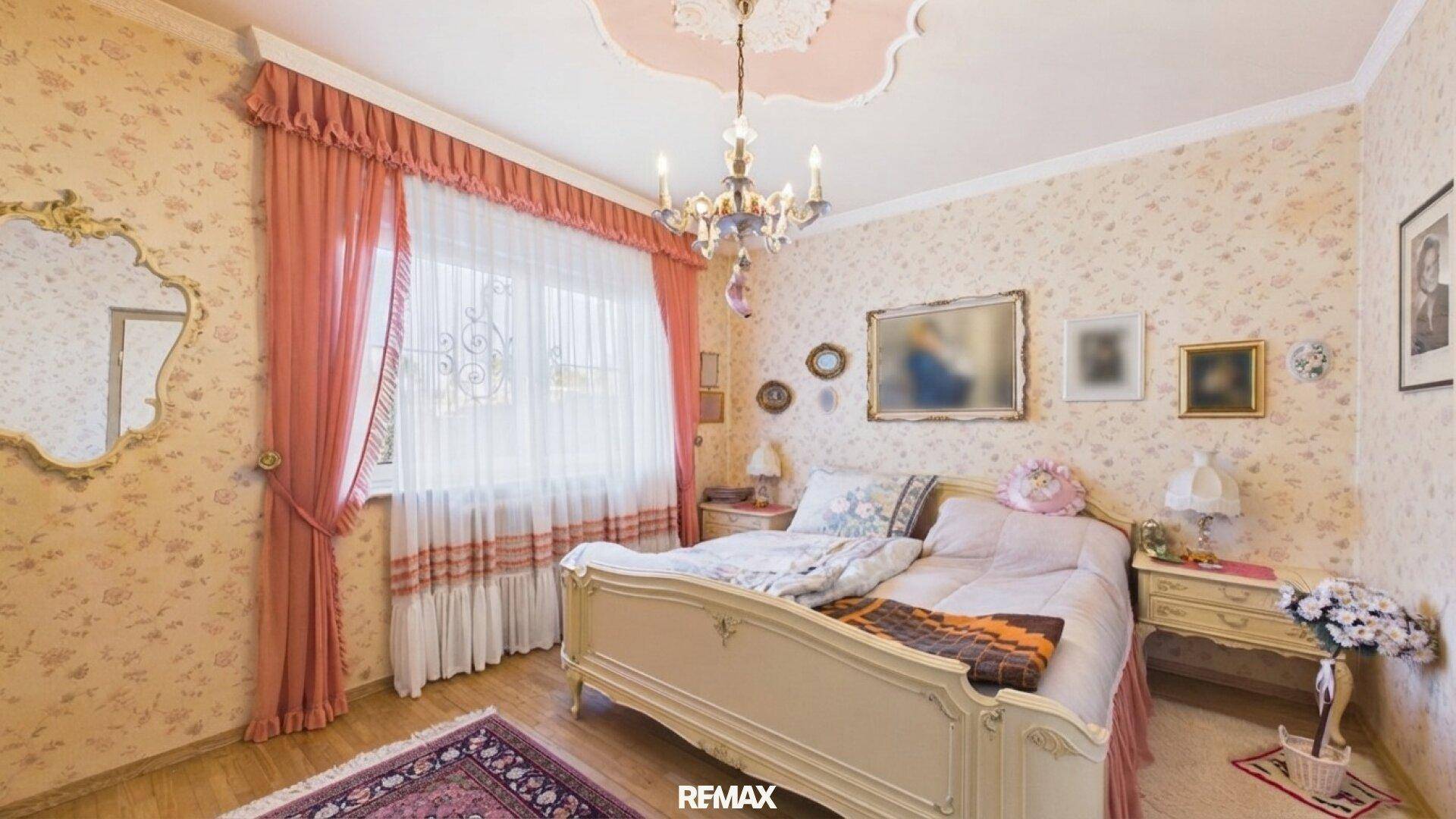 Schlafzimmer mit floraler Tapete, Stuckdecke und klassischem Bettgestell in Pastelltönen.