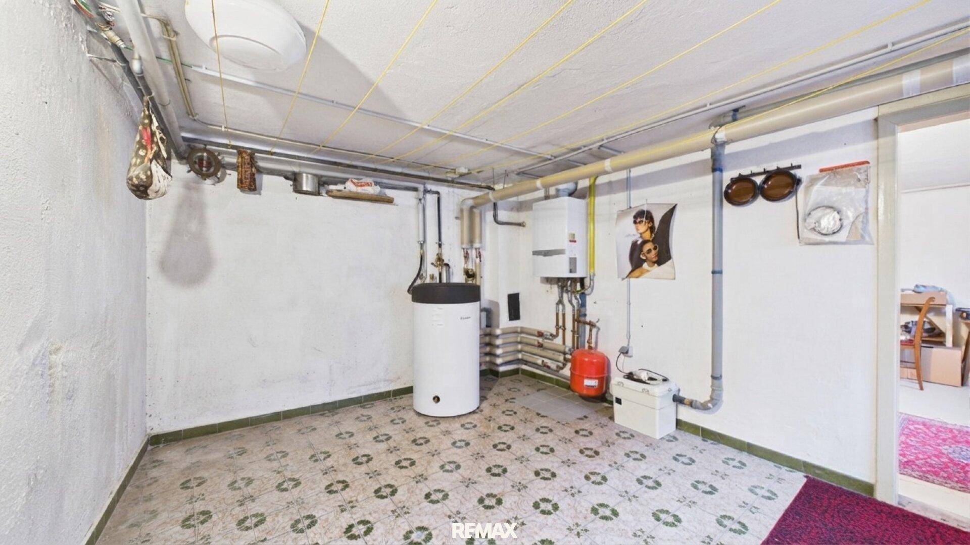 Heizungsraum im Keller mit Warmwasserspeicher, Rohren und Fliesenboden.