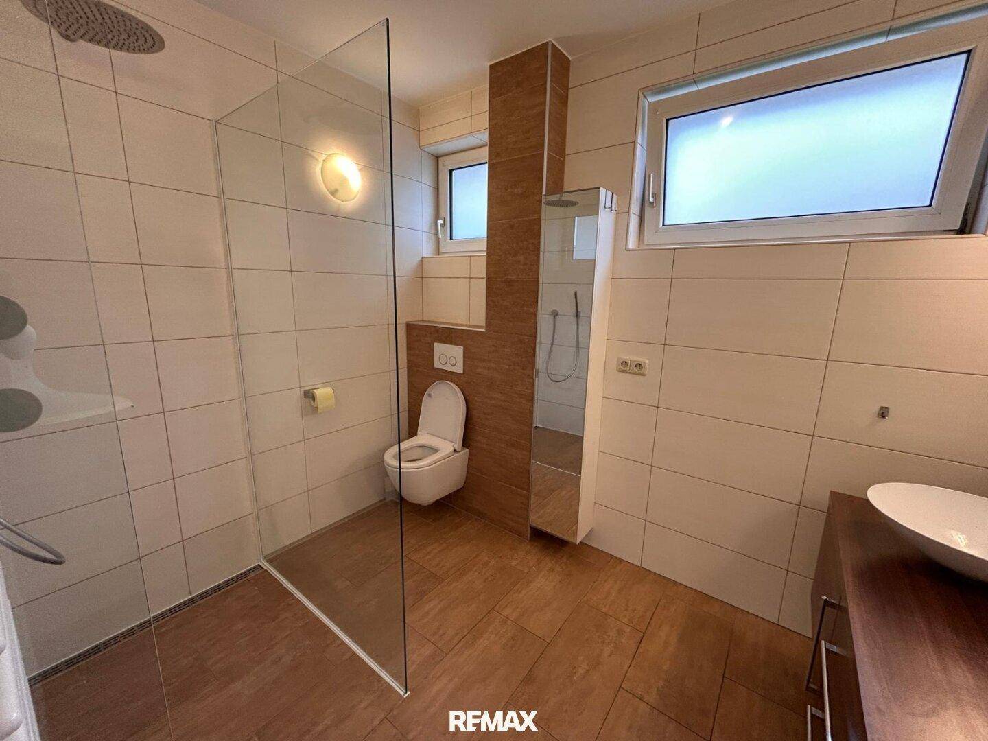 Modernes Badezimmer mit begehbarer Dusche, Wand-WC und Fenster, in warmen Erdtönen gefliest.